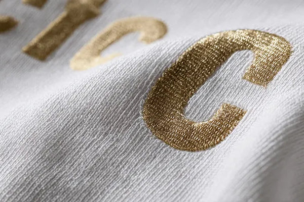 A close-up of the pattern on a gold-embroidered sweater. Embroidery, screen printing, heat transfer, foil, or silicone printing are also available