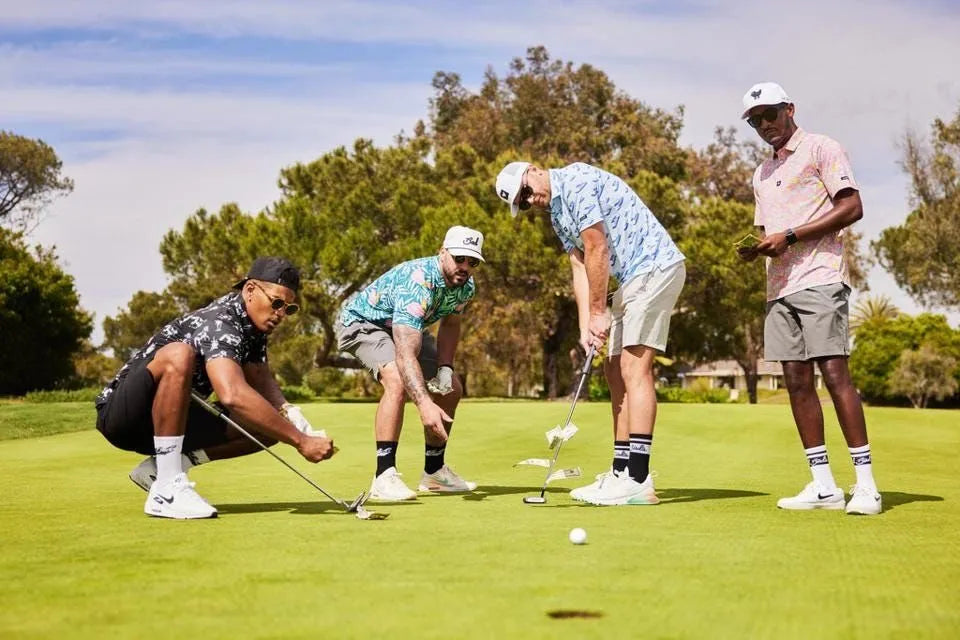 Four men playing golf on a green course with trees and a clear sky in the background.