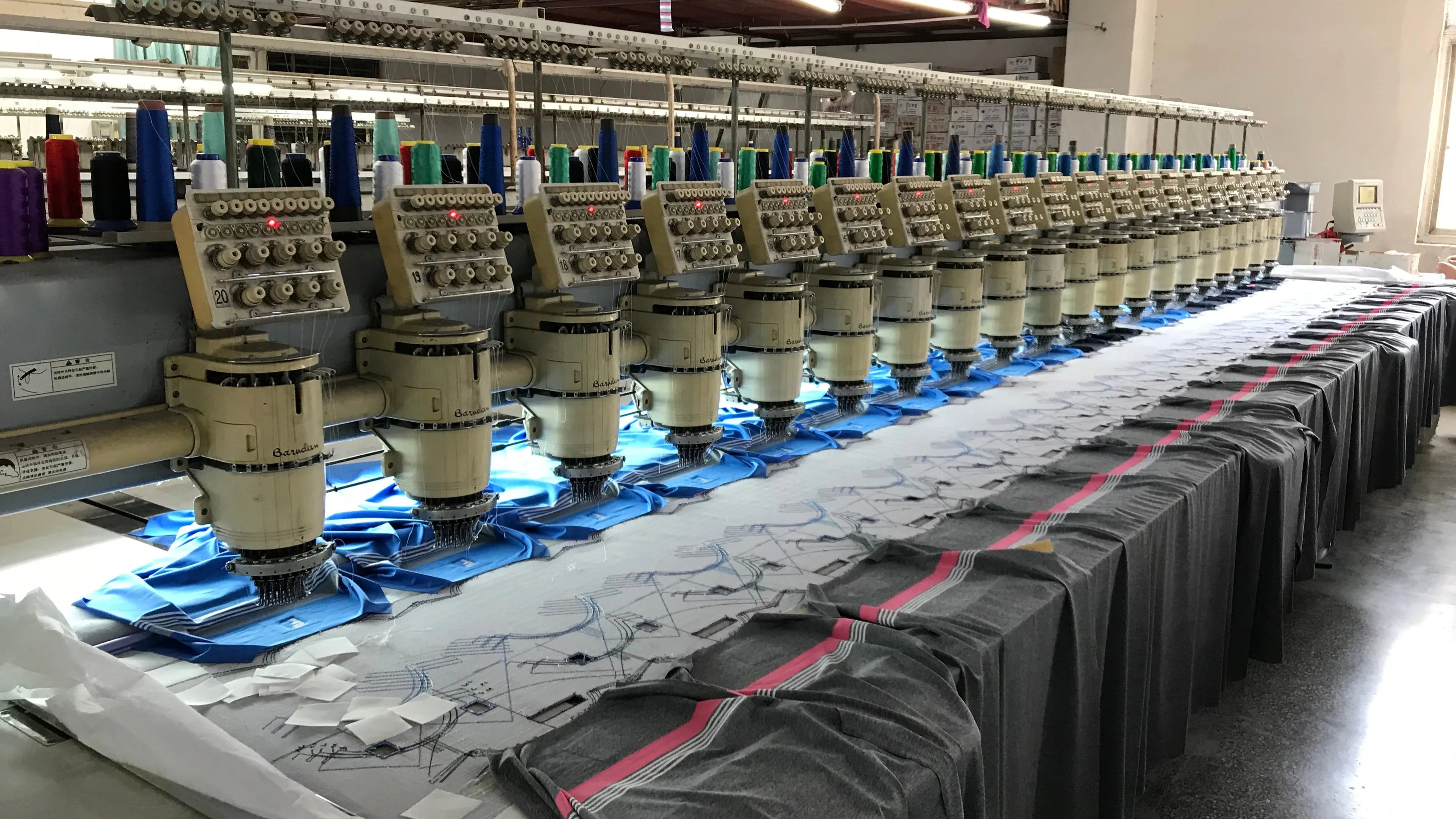 A row of industrial embroidery machines in a factory setting. This scene is a microcosm of the daily production process in the factory, symbolizing the steady progress in 2008